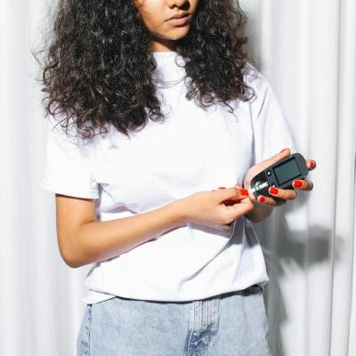 Eine junge Frau in weißem T-Shirt die gerade ihren Blutzucker misst